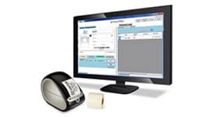 A desktop computer monitor displays shipping label software integrated with a Visitor Management System. Beside the monitor, a label printer is actively printing a shipping label, with a roll of blank labels placed nearby.